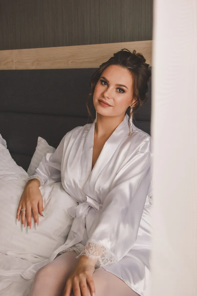 Woman seated on a bed wearing a pale robe with lace-trim cuffs